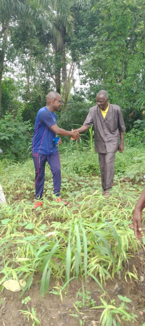 Two community members shaking hands over a field of crops