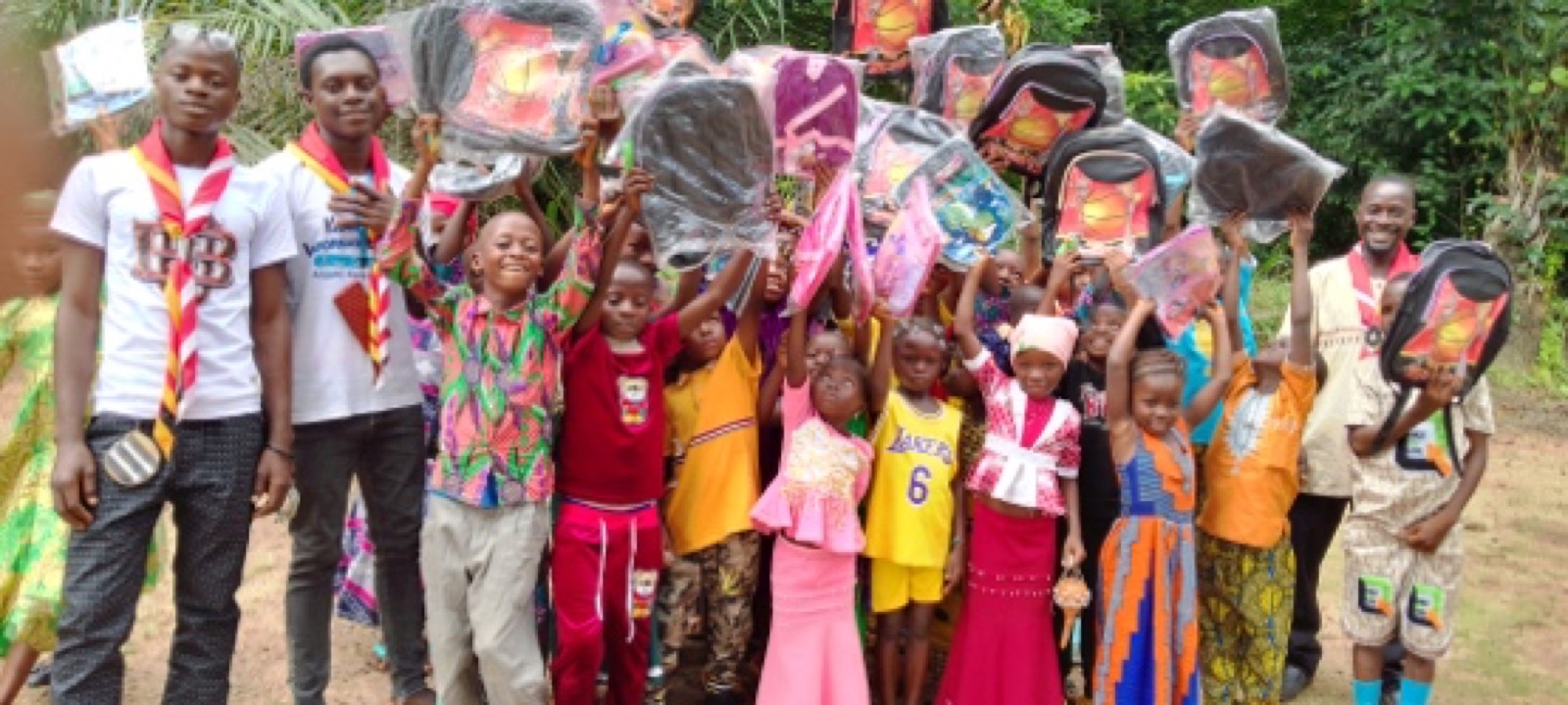 Children and community leaders in Guinea celebrating together, holding resources provided by the Trust