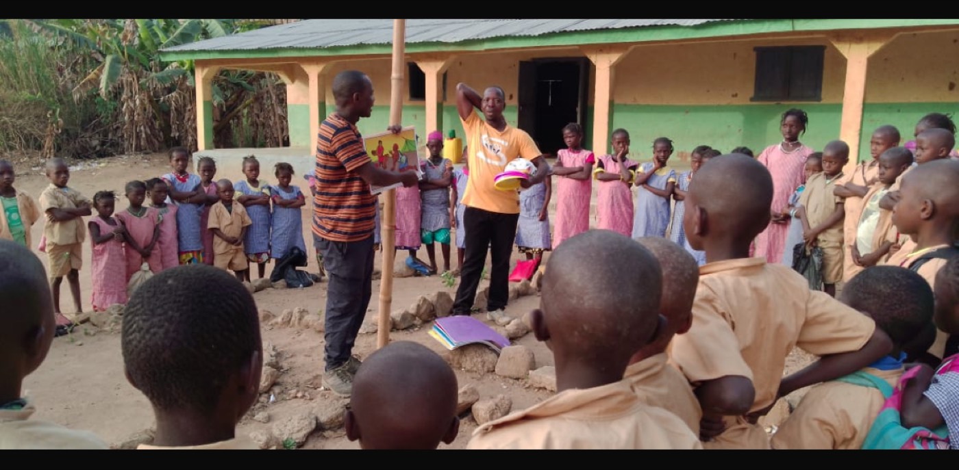 A teacher leading a lesson with pupils outside the Millimou school building